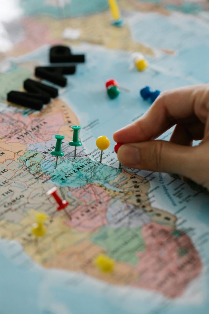 Close-up of hand marking locations on a map with colorful pins, planning a journey.